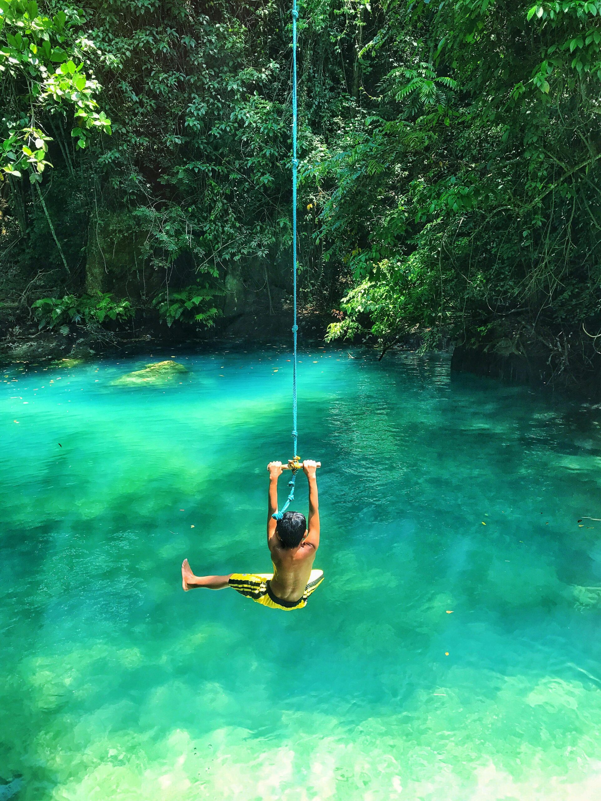 A child swinging joyfully on a rope over a stunning turquoise tropical lagoon.